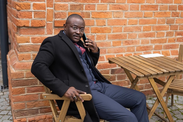 stylowy afrykański mężczyzna dzwoniący przez telefon na tle ceglanego muru