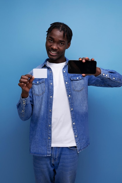Stylowy amerykański mężczyzna z czarnymi dredami trzymający makietę karty pieniężnej i smartfon