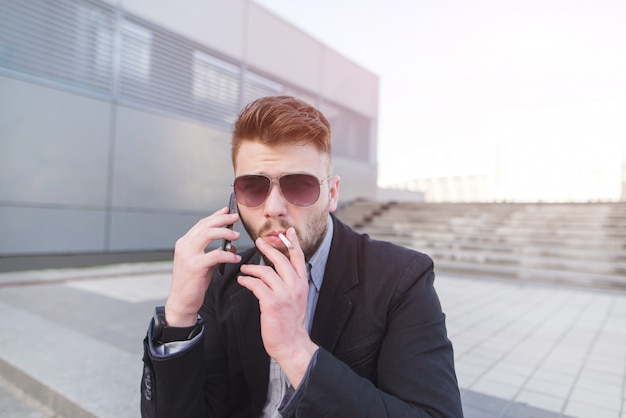 Stylowy Biznesmen Rozmawia Przez Telefon I Pali Papierosa.