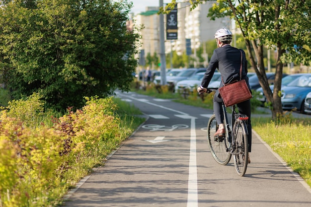 Zdjęcie stylowy biznesmen w kasku na rowerze na ścieżce rowerowej w słoneczny dzień