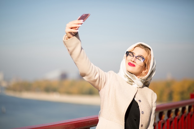 Stylowy blond model turystyczny biorąc selfie na smartfonie. Kobieta nosi szal i okulary