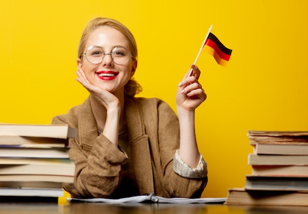 Zdjęcie stylowy blondynki kobiety obsiadanie przy stołem z książkami i flaga niemcy na kolorze żółtym
