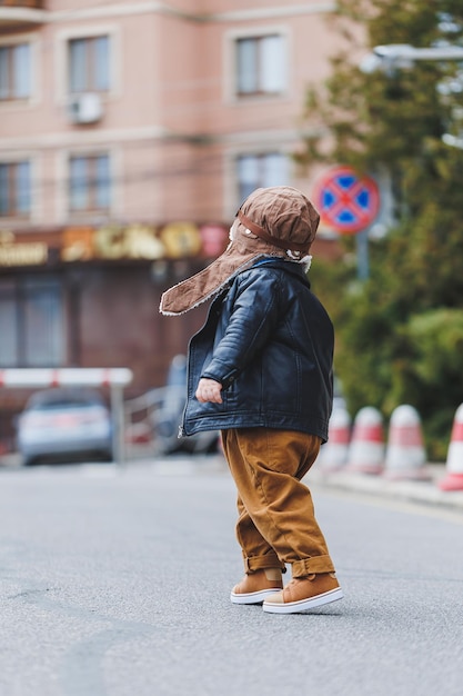 Stylowy chłopiec 3 lata w skórzanej kurtce i brązowych spodniach spaceruje po ulicy Nowoczesne dziecko Moda dziecięca Szczęśliwe dziecko