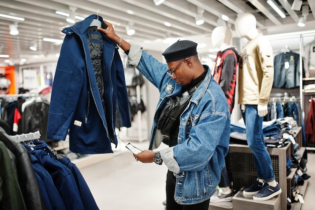 Stylowy dorywczo afroamerykanin w dżinsowej kurtce i czarnym berecie w sklepie z ubraniami, patrzący na nową kurtkę