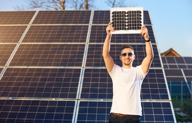 Stylowy facet trzyma panel słoneczny nad sobą W tle są rzędy paneli słonecznych na sąsiednich obszarach