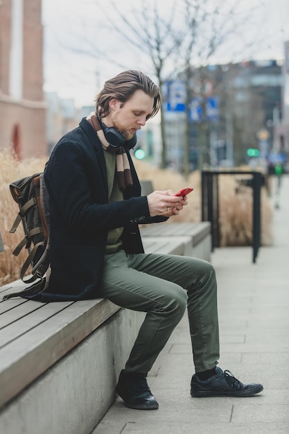 Stylowy facet w szaliku i płaszczu trzyma telefon komórkowy w dłoni na ulicy Wrocław Polska