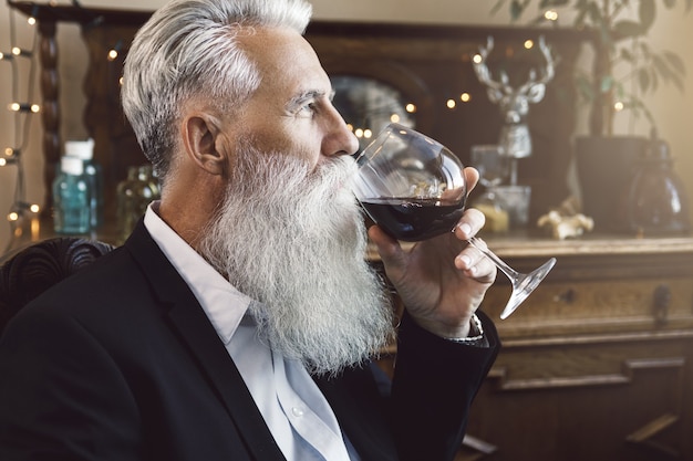 Stylowy i przystojny brodaty starszy mężczyzna pije czerwone wino