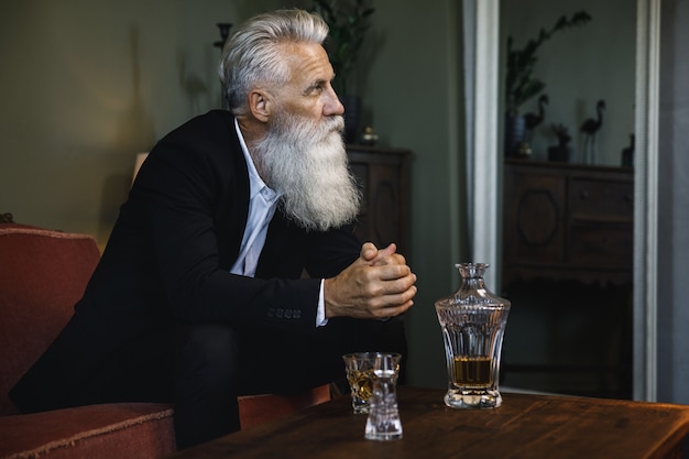 Stylowy i przystojny brodaty starszy mężczyzna pije whisky