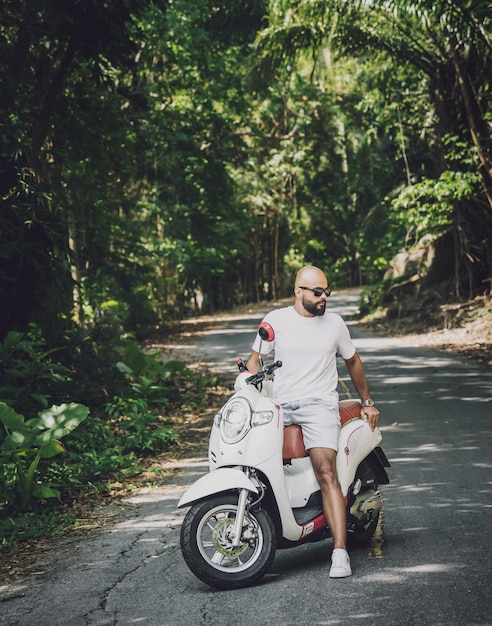 Stylowy młody człowiek i jego motocykl na drodze w dżungli