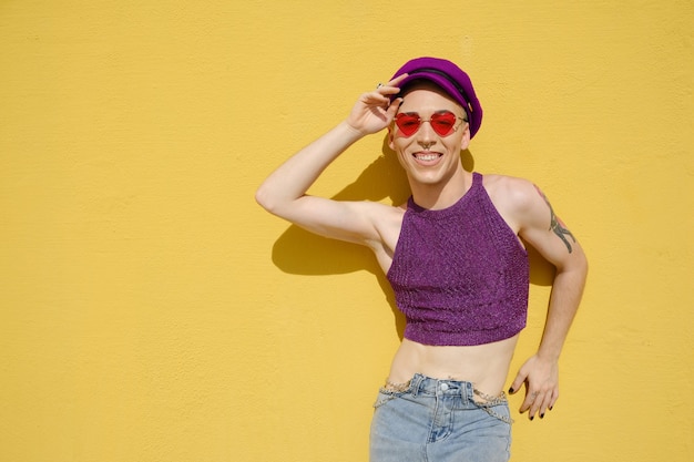 Stylowy młody niebinarny model pozowanie na zewnątrz w słoneczny dzień na żółtej ścianie. Tożsamość płciowa i koncepcja niebinarna.