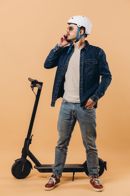Stylowy współczesny mężczyzna w kasku stoi przy hulajnodze i rozmawia przez telefon