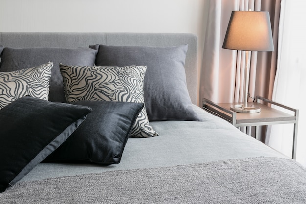 Stylowy wystrój sypialni z czarnymi wzorzystymi poduszkami na łóżku i dekoracyjną lampą stołową.