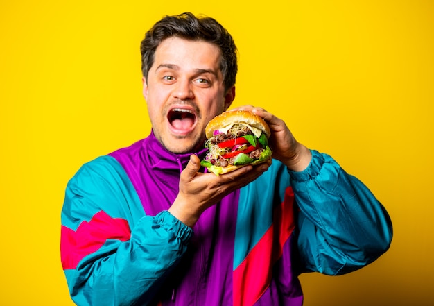 Styluj faceta w ubraniach z lat 80. z dużym burgerem na żółtej przestrzeni