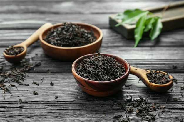 Suche liście czarnej herbaty w miseczkach i łyżkach na drewnianym stole