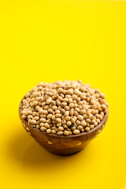 Suche nasiona soi w drewnianej misce na żółtym tle