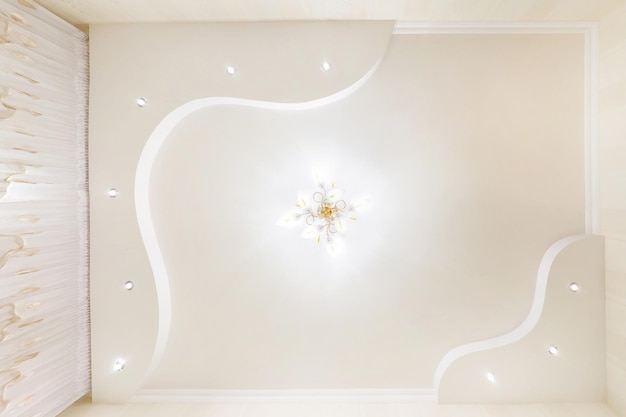 Sufit napinany biały i złożony kształt z halogenowymi lampami punktowymi i konstrukcją płyt kartonowo-gipsowych w pustym pomieszczeniu w mieszkaniu lub domu Sufit podwieszany