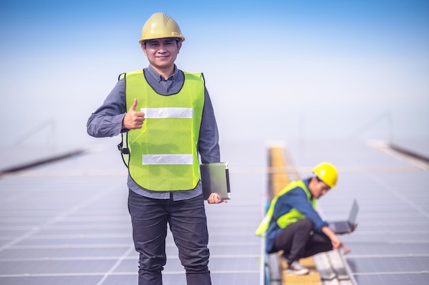 Sukces pracy zespołowej azjatyckiego inżyniera, stojący szczęśliwie w pracy, instaluje się na dachu fabryki energii słonecznej energii ogniw słonecznych