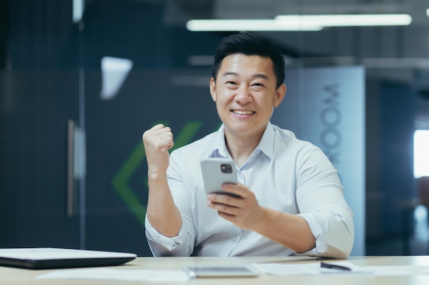 Sukces wygraj młody azjatycki biznesmen trzyma telefon w ręku raduje się wygraj dobre wieści czyta wiadomość