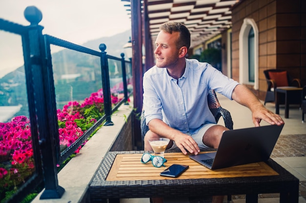 Sukcesy biznesmen siedzi przy stole z laptopem pracuje na wakacjach Wakacje i praca zdalna Facet siedzi w restauracji na tarasie z panoramicznym widokiem