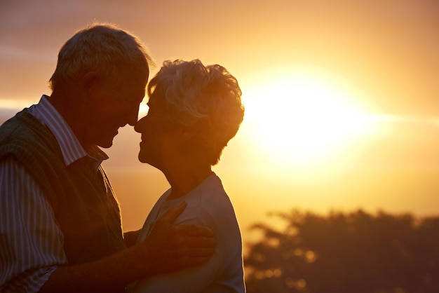 Zdjęcie sunset starsza para i uścisnąć w naturze opieka i więź dla połączenia razem na świeżym powietrzu mężczyzna kobieta i dotyk nosa dla miłości romans i wsparcie dla zaangażowania w związek na emeryturze