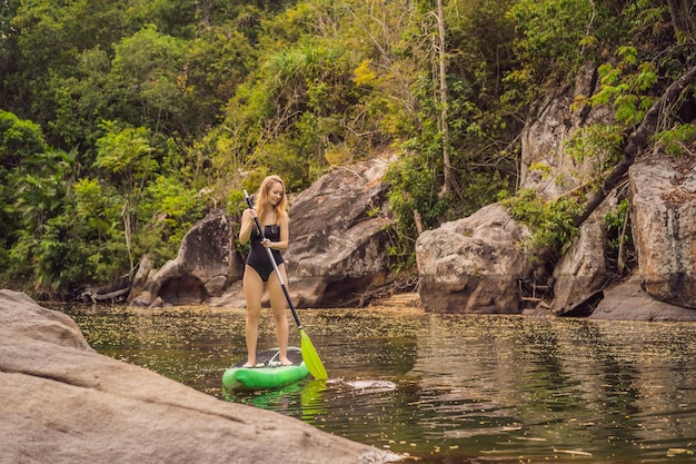 SUP Stand up paddle board kobieta wiosłująca na pokładzie jeziora stojąca szczęśliwa na desce wiosłowej na niebieskiej wodzie Zdjęcie młodej kobiety na desce wiosłowej