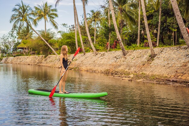 SUP Stand Up Paddle Board kobieta wiosłująca na pokładzie jeziora stojąca szczęśliwa na paddleboardzie na niebieskiej wodzie Zdjęcie młodej kobiety na desce wiosłowej