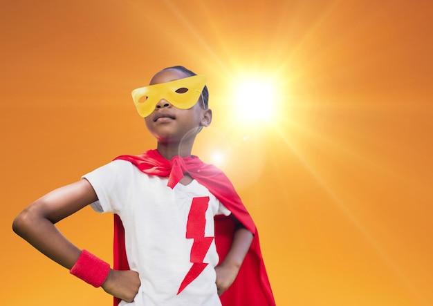 Super dzieciak w czerwonej pelerynie i żółtej masce stojący z ręką na biodrze przed jasnym światłem słonecznym