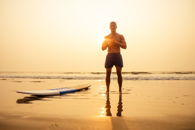 Surfer fitness mężczyzna o muskularnym ciele z deską surfingową na plaży rozgrzewki