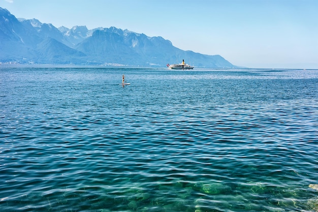 Surfer na desce do wiosłowania i statek wycieczkowy na Jeziorze Genewskim w Montreux, Riwiera Szwajcarska