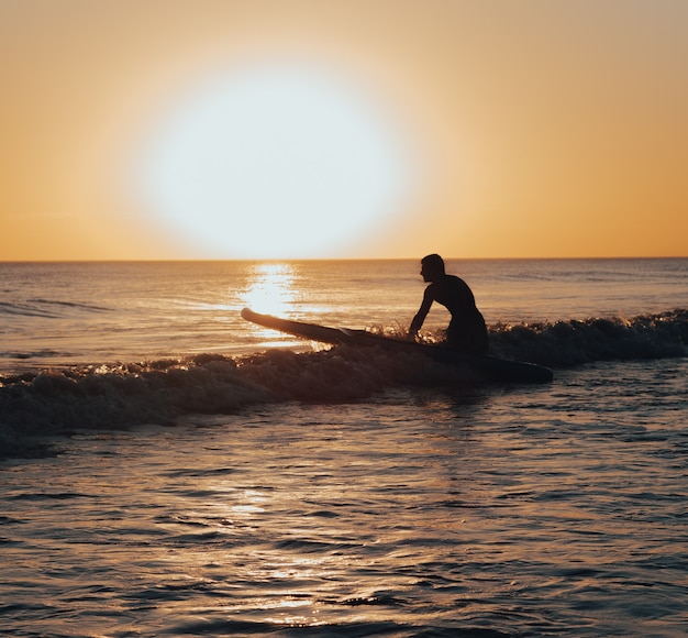 Surfer przygotowuje się do surfowania po morzu o zachodzie słońca