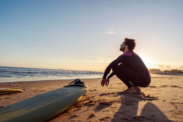 Surfer przykucony na brzegu i patrzący na ocean