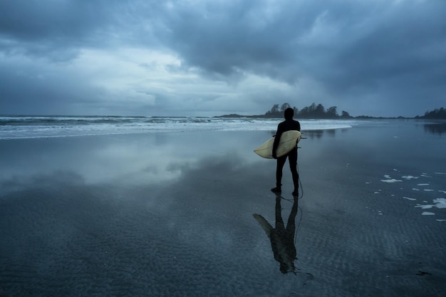 Surfer wyrusza w ocean podczas pochmurnego zimowego zachodu słońca