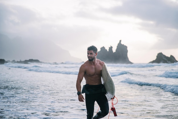 Surfer z deską surfingową spaceruje po plaży atrakcyjny facet rozgląda się