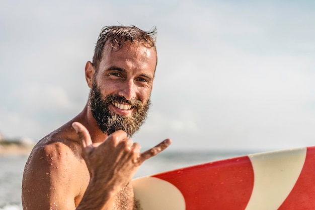 Surfer zadowolony z surfowania uśmiecha się, robiąc hawajskiego Shaka Brah lub Hang Loose