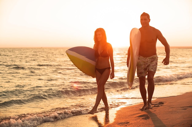Surferzy płci męskiej i żeńskiej na piaszczystej plaży o zachodzie słońca