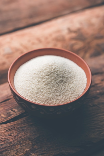Surowa, nieprzygotowana mąka z kaszy manny, znana również jako proszek Rava w języku hindi, w misce lub łyżce. zbliżenie na białym lub nastrojowym tle. selektywne skupienie