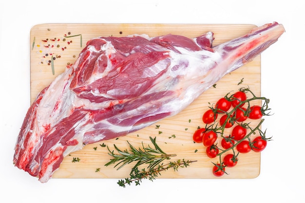surowa noga jagnięca, schab na kości z ziołami, deska do krojenia mięsa, na białym, izolowanym tle