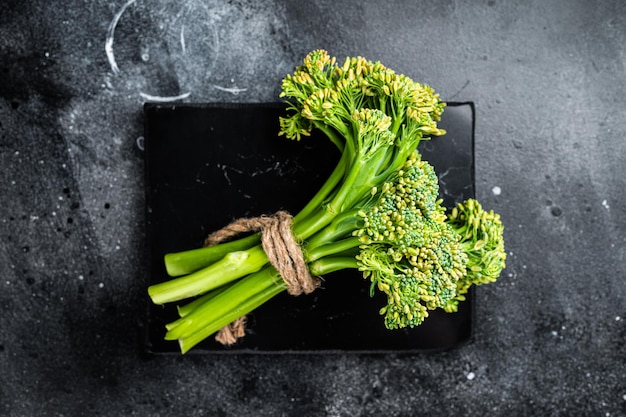 Surowa zielona gałąź Broccolini na marmurowej desce Czarne tło Widok z góry