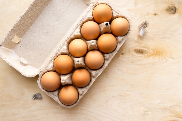 Surowe brązowe jaja kurze w tekturowym pudełku na drewnianym tle, widok z góry.
