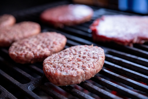 Zdjęcie surowe burgery wołowe ze szczyptą soli i czarnego pieprzu na grillu. gotowe mięso do grillowania. surowe kotlety burgerowe. okrągłe placki z surowego mięsa mielonego pieczone na metalowej kratce.