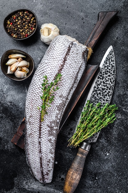 Surowe grenadier macrurus białe ryby na drewnianej desce do krojenia. Czarne tło. Widok z góry.