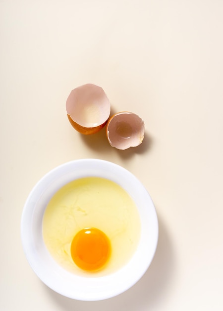 Surowe jajka i skorupka jajka w szklanej misce na stole Widok z góry złamane białe tło