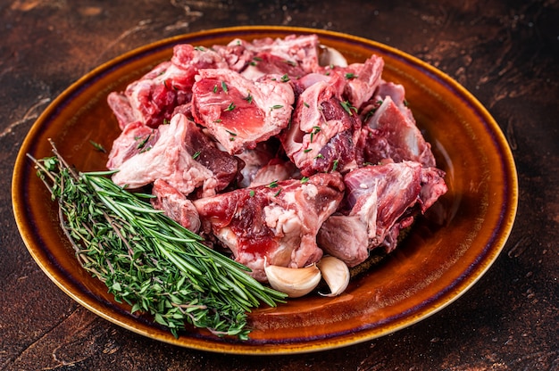 Surowe mięso baranie pokrojone w kostkę na gulasz lub gulasz z kością na rustykalnym talerzu. Ciemny