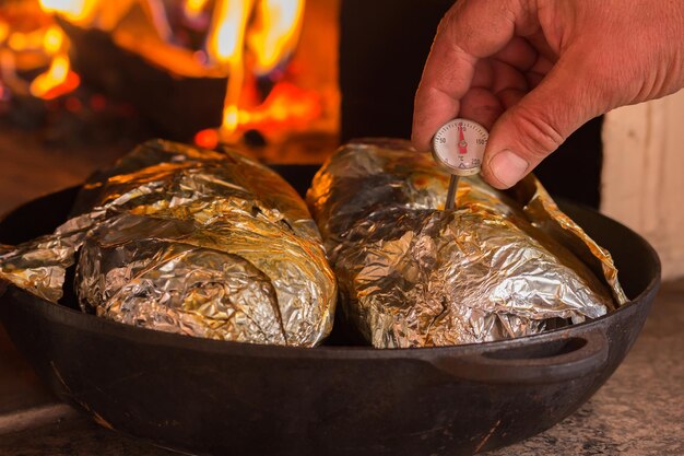 Surowe mięso na żeliwnej patelni stoi przed piecem opalanym drewnem Patelnia obok płonącego ognia Proces gotowania Seria zdjęć