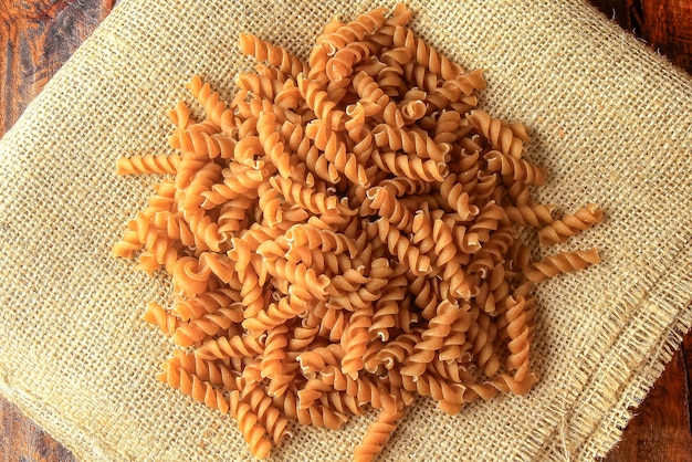 Surowe pełnoziarniste makarony fusilli na rusztycznej tkaninie na drewnianym stole