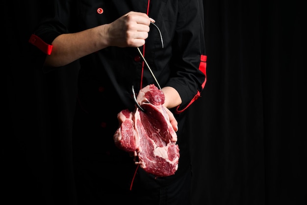 Surowe steki na haczyku mięsnym w rękach szefa kuchni Mięso na czarnym tle
