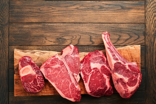 Surowe steki Prime Różnorodność świeżych steków mięsnych Black Angus Prime Tbone New York Ribeye Striploin Tomahawk deska do krojenia na czarnym lub ciemnym tle Zestaw różnych klasycznych steków Widok z góry