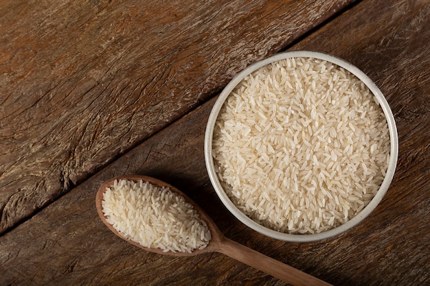 Surowy biały ryż w ceramicznej misce na brązowym drewnianym tle