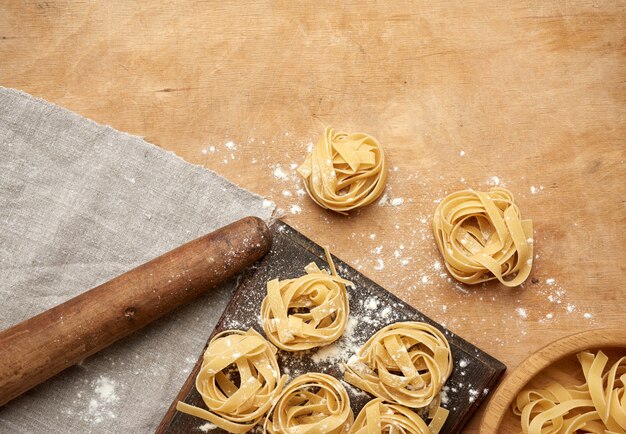 Surowy makaron fettuccine na brązowej desce i drewnianym vintage wałkiem do ciasta