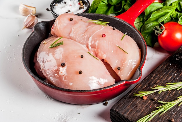 Zdjęcie surowy świeży filet z piersi kurczaka z ziołami i przyprawami do gotowania, na patelni żeliwnej, stół z białego marmuru, copyspace